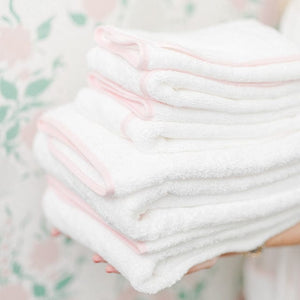 A model holds a stack of white towels with light pink piping.